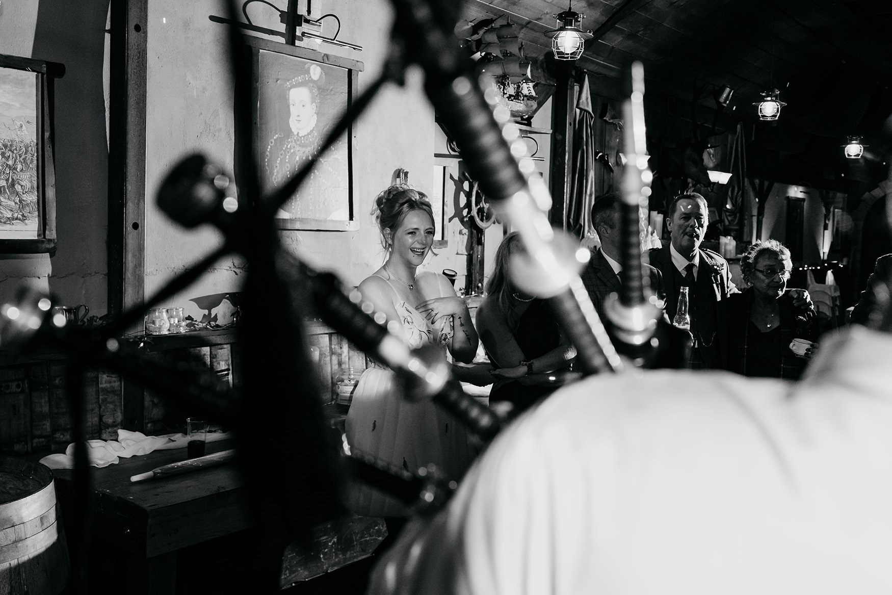 black and white photograph of bride smiling, taken through grooms bagpipes at The Gathering at Woodhead Farm